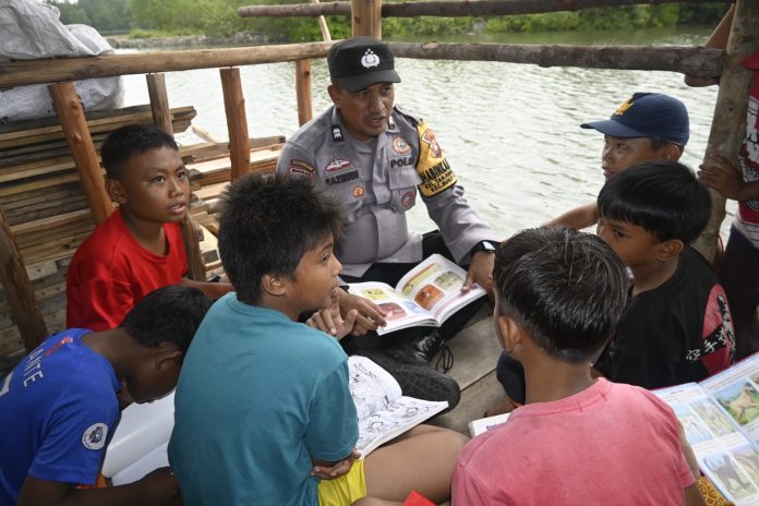 Bhabinkamtibmas Kelurahan Tanjung Unggat Aiptu Razmudi saat membaca buku bersama anak-anak Plantar Tanah Merah, Kelurahan Tanjungunggat. Polsek Bukit Bestari Polresta Tanjungpinang distribusikan 350 buku di Pondok Baca Presisi, Kamis, (7/9) f,Polsek Bukit Bestari