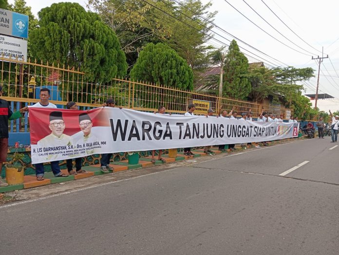 Warga Tanjung Unggat, Kecamatan Bukit Bestari, Kota Tanjungpinang, menggelar aksi dukungan untuk pasangan calon Wali Kota dan Wakil Wali Kota Tanjungpinang, Lis Darmansyah-Raja Ariza (Lis-Raja), dengan membentangkan spanduk sepanjang 30 meter di tepi Jalan Sultan Mahmud, Tanjung Unggat, Rabu (13/11/2024). F, tim Lis-Raja