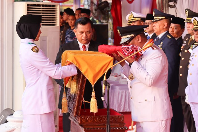 Wakil Gubernur Kepri, Nyanyang Haris Pratamura mencium bendera merah putih yang diserahkan Nurjihan Dwi Hanifah, Paskibraka yang bertugas membawa baki pada Upacara Penurunan Bendera Peringatan HUT ke-81 di Gedung Daerah, Tanjungpinang, Senin (17/8/2026). (Enji/DISKOMINFO KEPRI)
